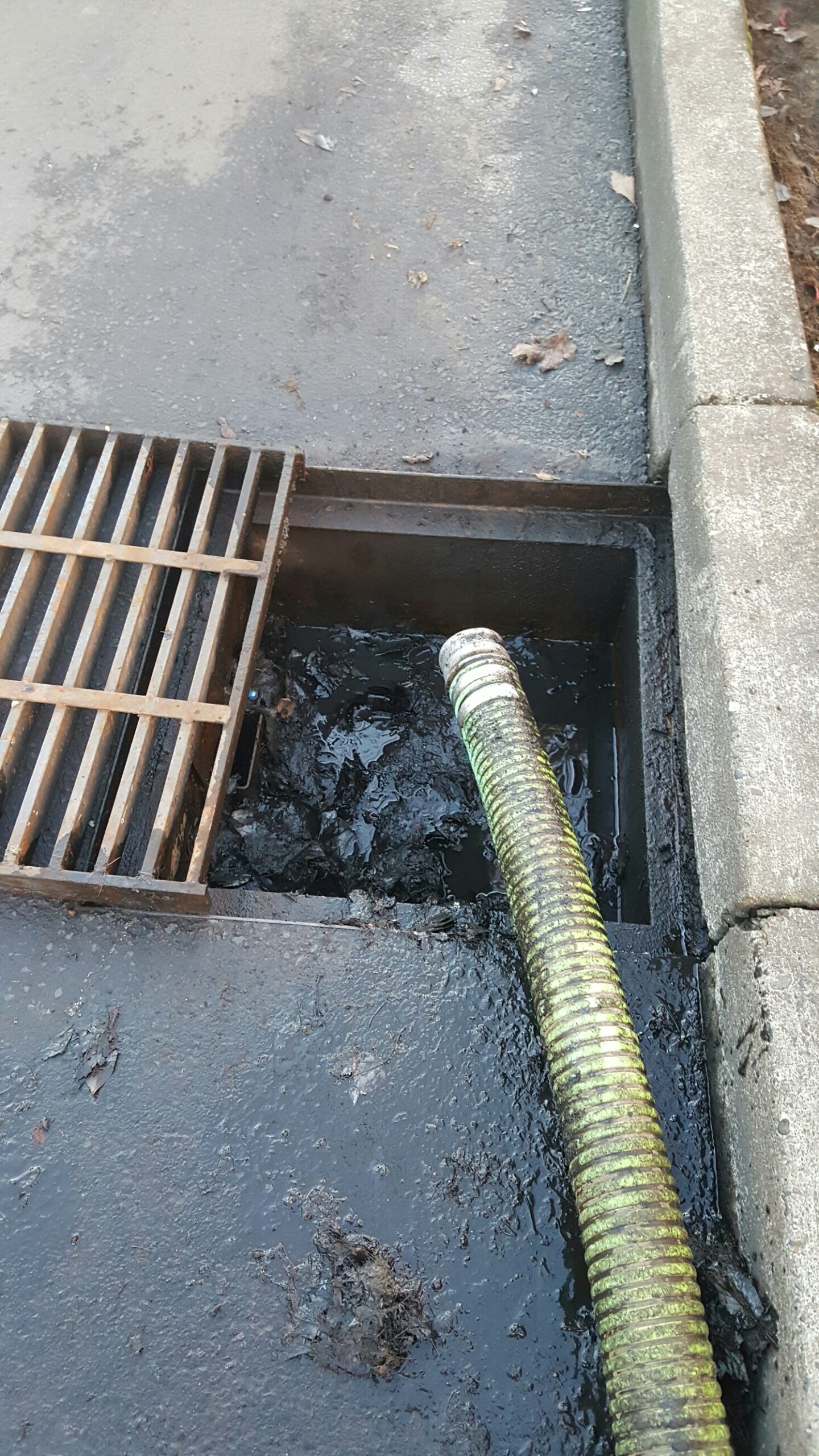 Sweep-Rite Pump Clearing Drain A green drain pump dipping into a road's sewer entrance